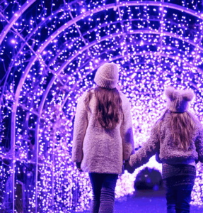 RHS Garden Wisley GLow with mum and child walking through a tunnel of festive lights 