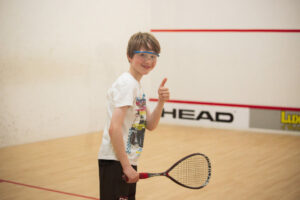 Boy playing squash at the oakwood Esher at holiday camps or weekly squash sessions for children and teens
